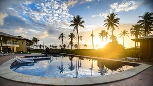 A swimming pool with lounge chairs, palm trees, and a building with balconies.