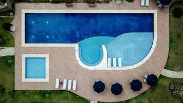Vista aerea di una zona piscina con una piscina rettangolare, una piscina più piccola e un’area relax con ombrelloni.