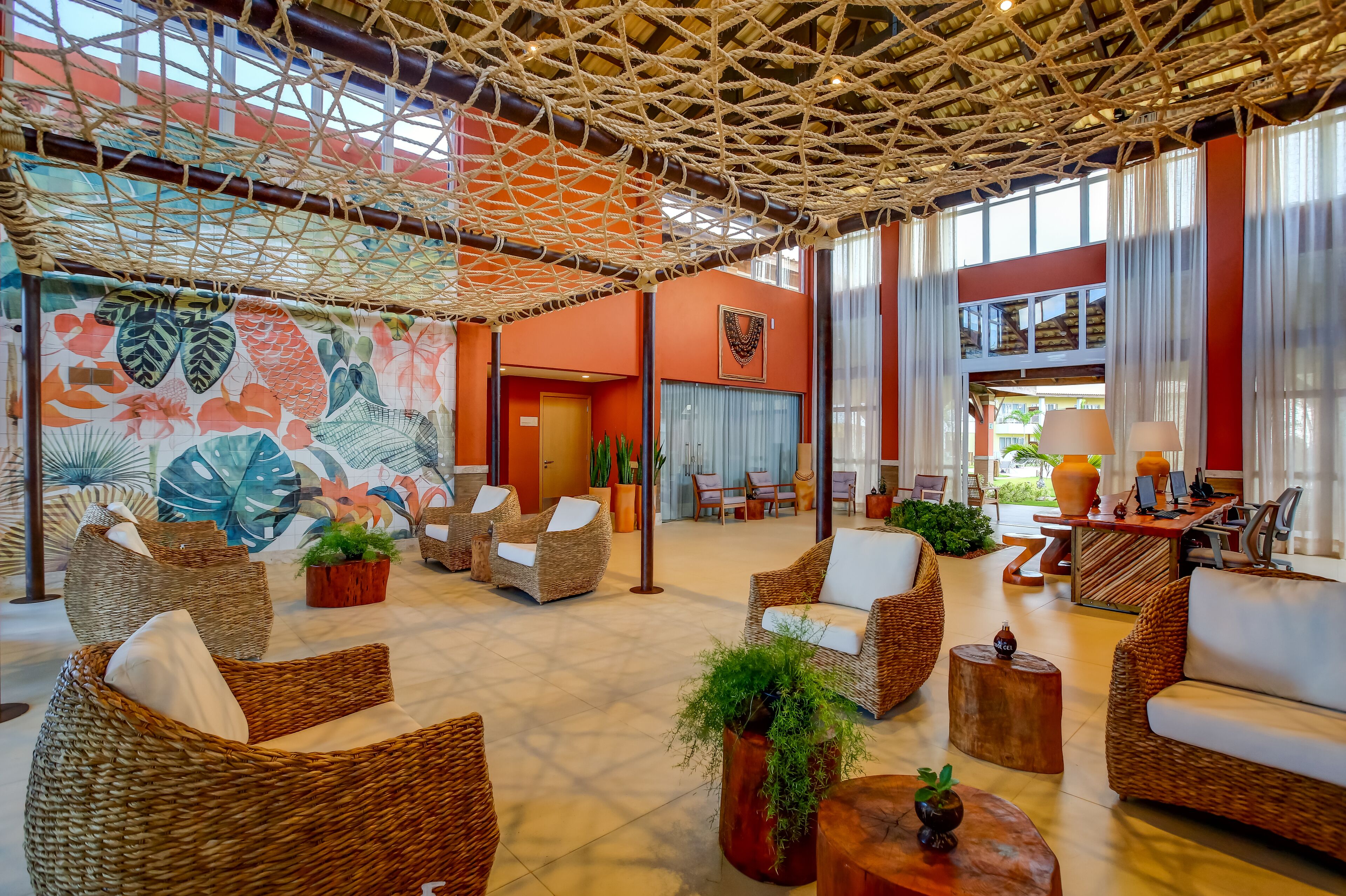 A spacious lobby with wicker furniture, a large mural, and a netted ceiling.