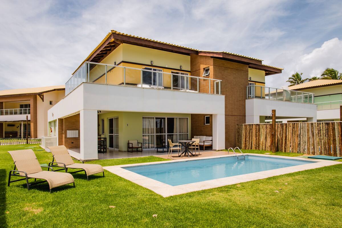 A two-story house with a swimming pool, outdoor seating, and a wooden fence.