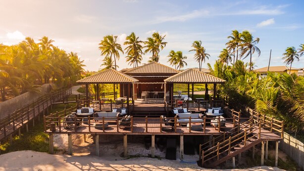 A beachside resort with outdoor seating areas, palm trees, and a sandy beach.