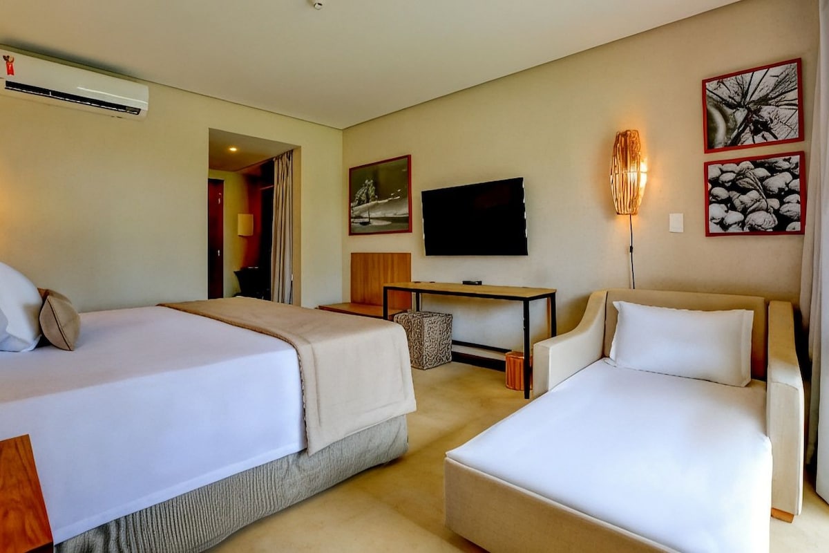 A hotel room with two beds, a TV, a desk, and artwork on the wall.