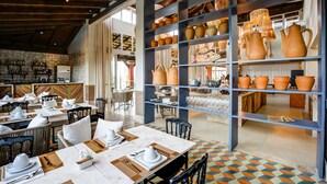 A restaurant with tables set for dining, a bar area, and shelves with pottery and glassware.