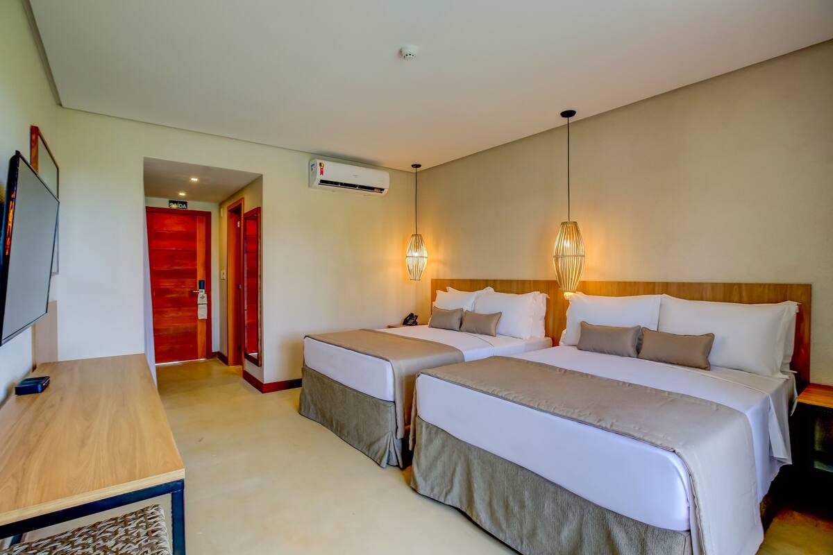 A hotel room with two beds, a desk, a TV, and an air conditioning unit.