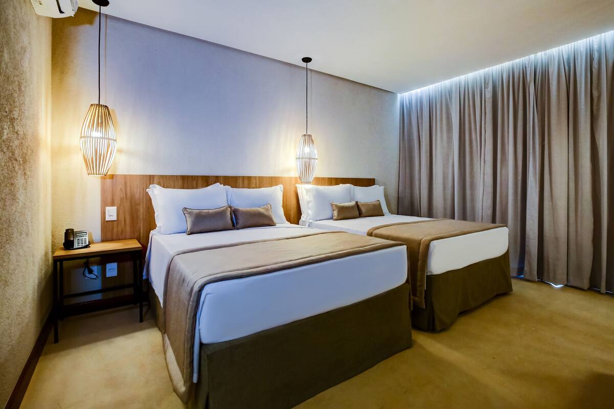 A hotel room with two beds, a bedside table with a phone, and a hanging light fixture.