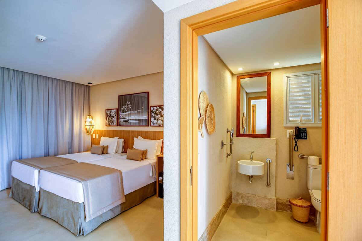 A hotel room with two beds, a bathroom with a sink and toilet, and a mirror.