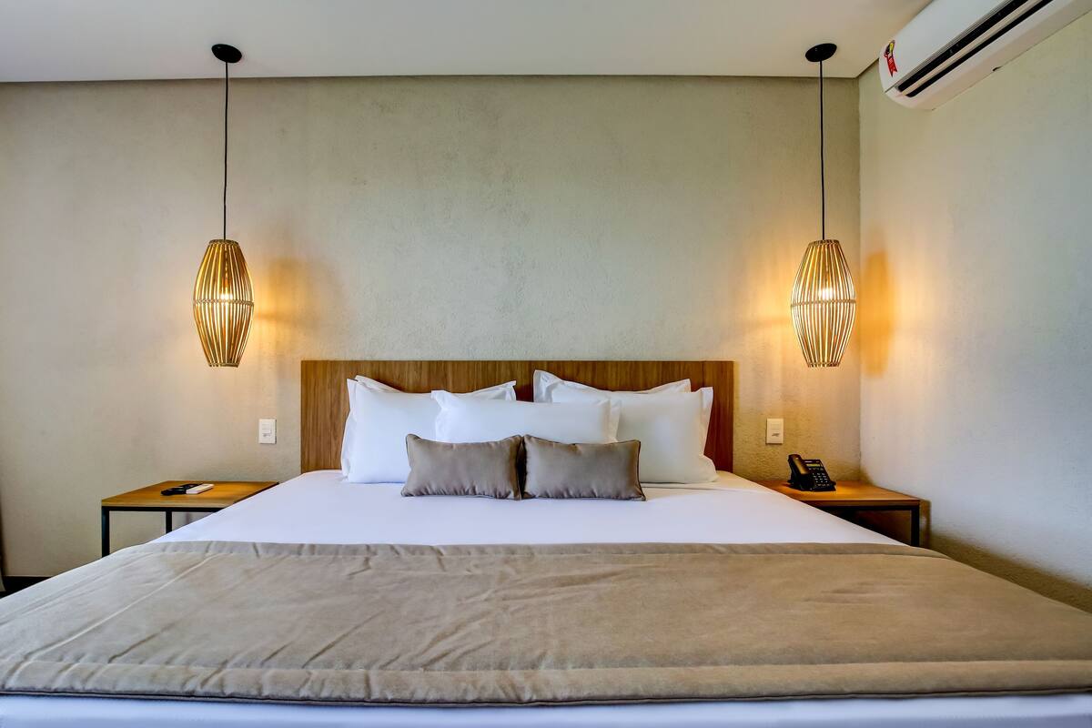 A hotel room with a large bed, two bedside tables, a telephone, and two pendant lights.