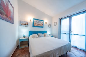 Quarto com cama, mesa de cabeceira, relógio na parede e janela com cortinas.