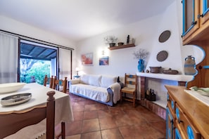 Uma sala de estar aconchegante com sofá, mesa de jantar e cadeiras. Há uma janela com vista para o verde lá fora.