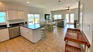 A spacious kitchen with a central island, dining area with chairs, and a living room with a sofa and TV.