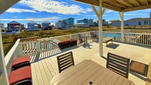 A covered deck with outdoor seating and a view of beach houses.