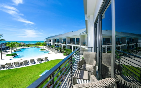 A hotel with a pool, lounge chairs, and a view of the ocean.