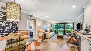 A modern living room with a sofa, chairs, a coffee table, and a TV. There is a kitchen area with cabinets and a countertop. - Anna Maria Beach Resort (Holmes Beach)
