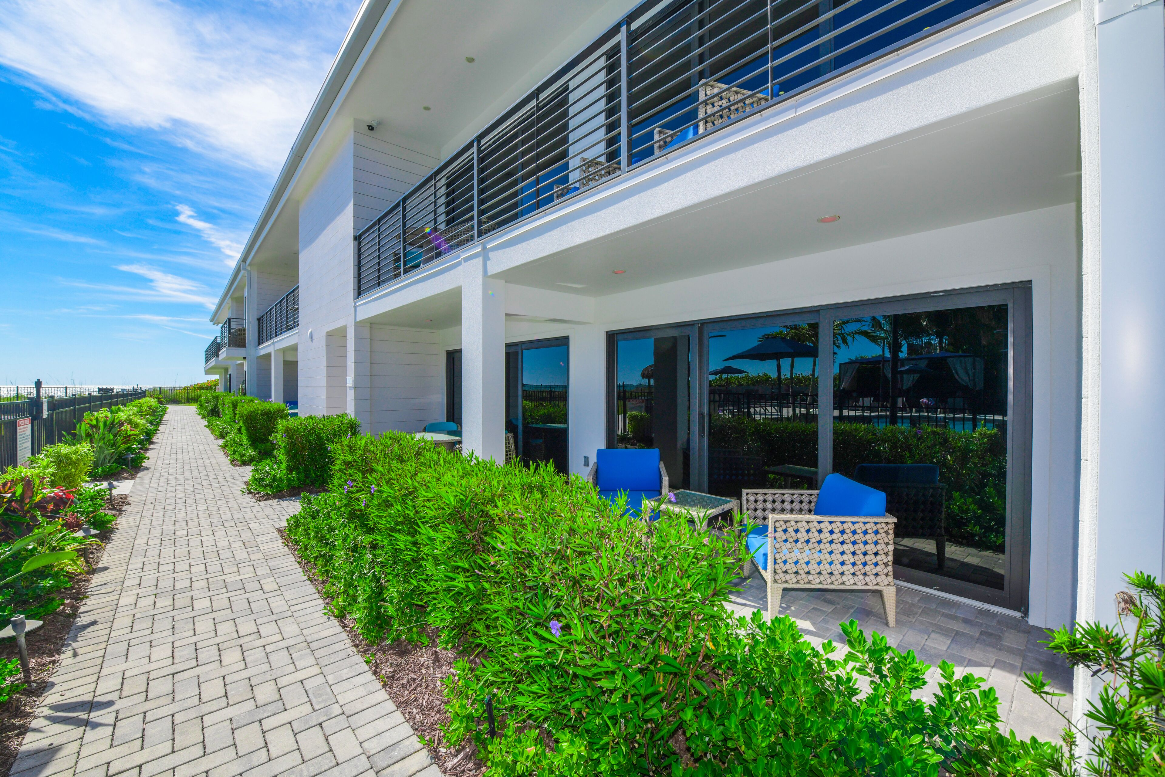 A modern building with a paved walkway, outdoor seating, and lush greenery.