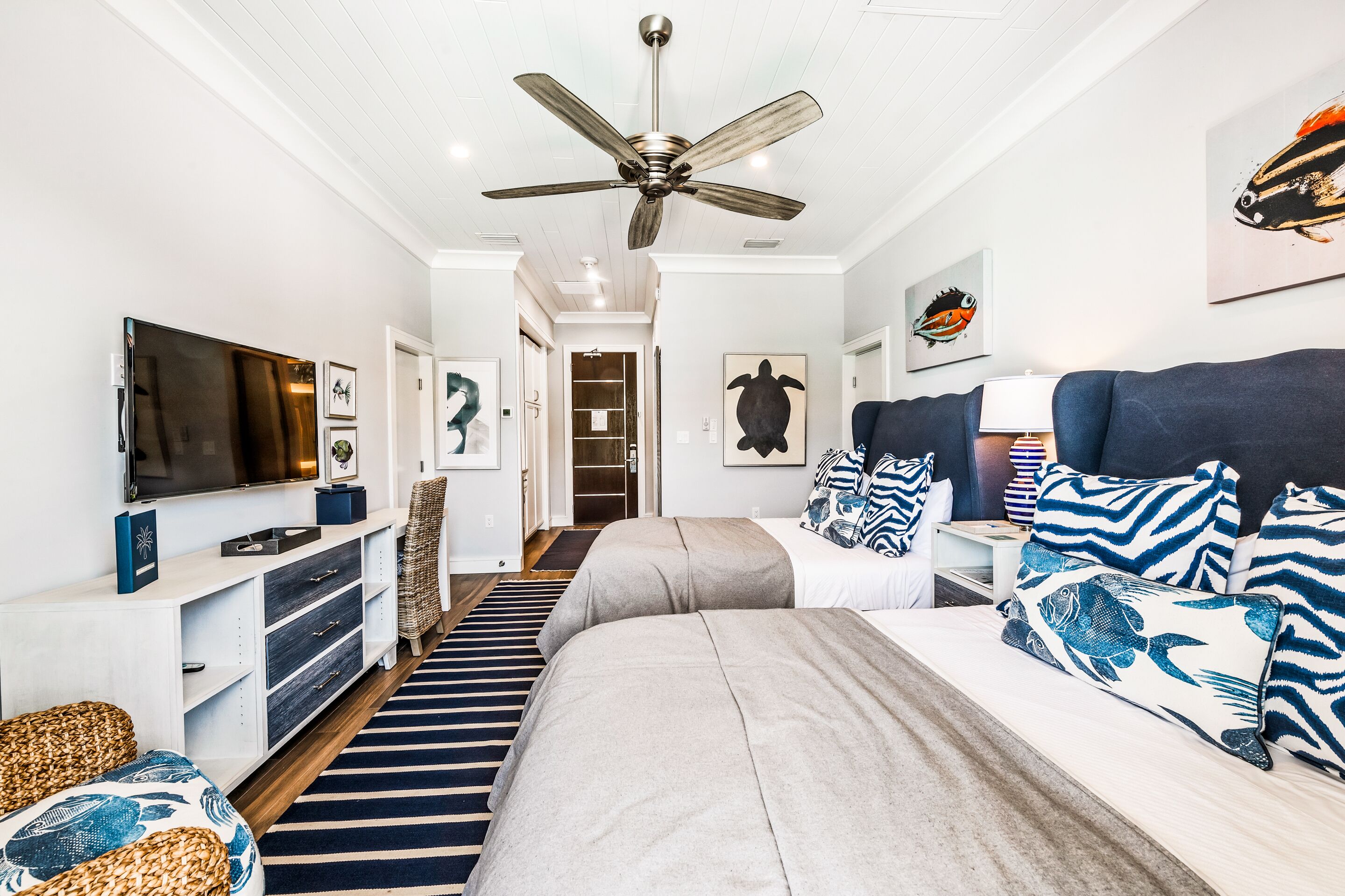 A modern bedroom with a large bed, a TV, a ceiling fan, and artwork on the walls.