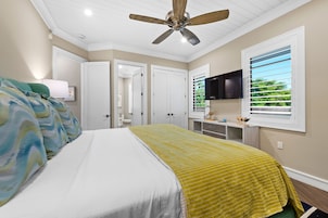 Une chambre à coucher avec un lit, un ventilateur de plafond, une télévision et une fenêtre avec des stores.