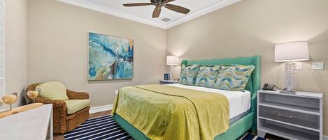 A bedroom with a bed, a ceiling fan, a nightstand, a lamp, a chair, and a painting on the wall.