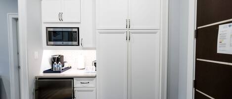 A compact kitchen with white cabinetry, a built-in microwave, and a small refrigerator.