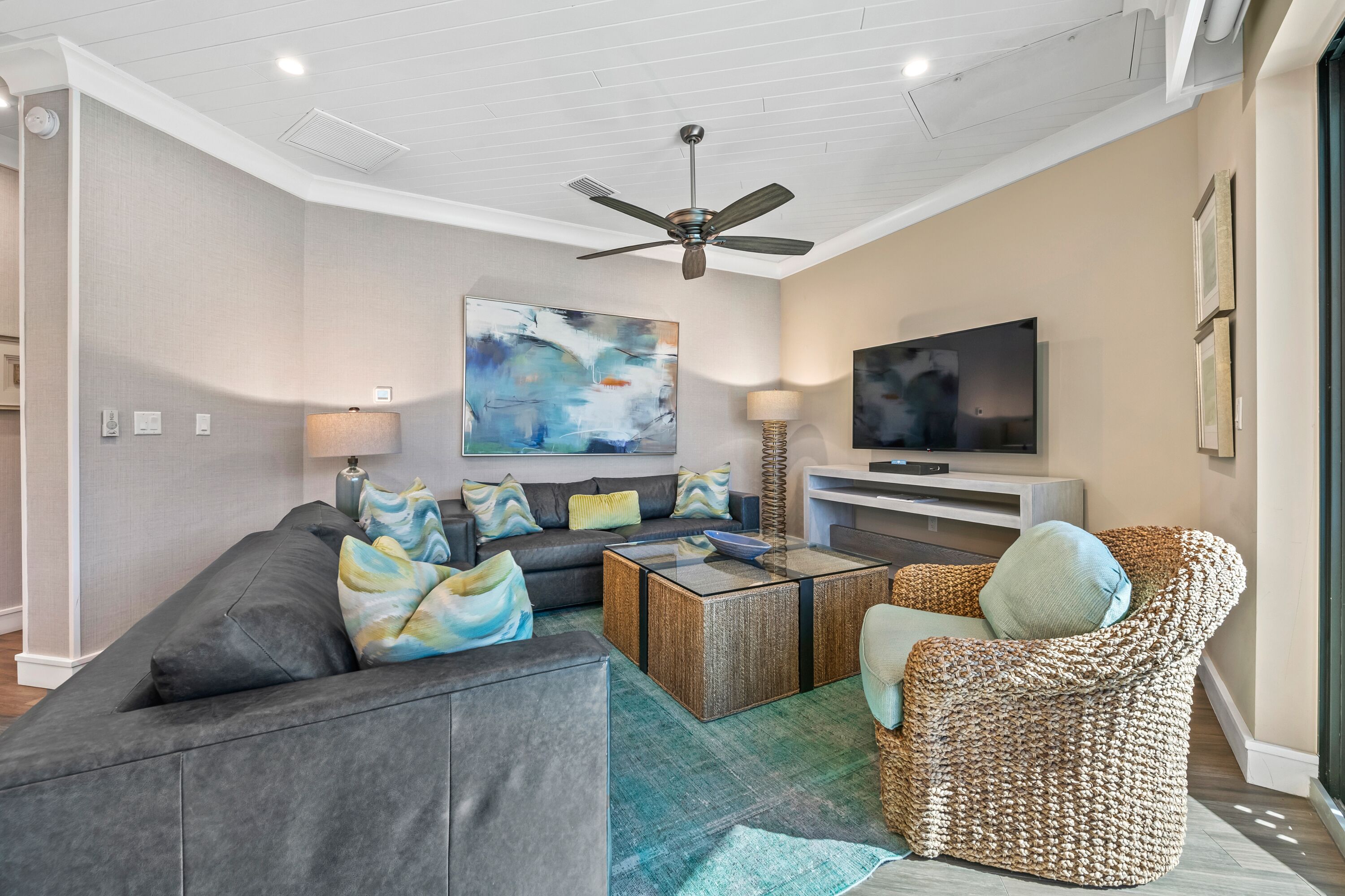 A modern living room with a grey sofa, a woven armchair, a coffee table, and a flat-screen TV.
