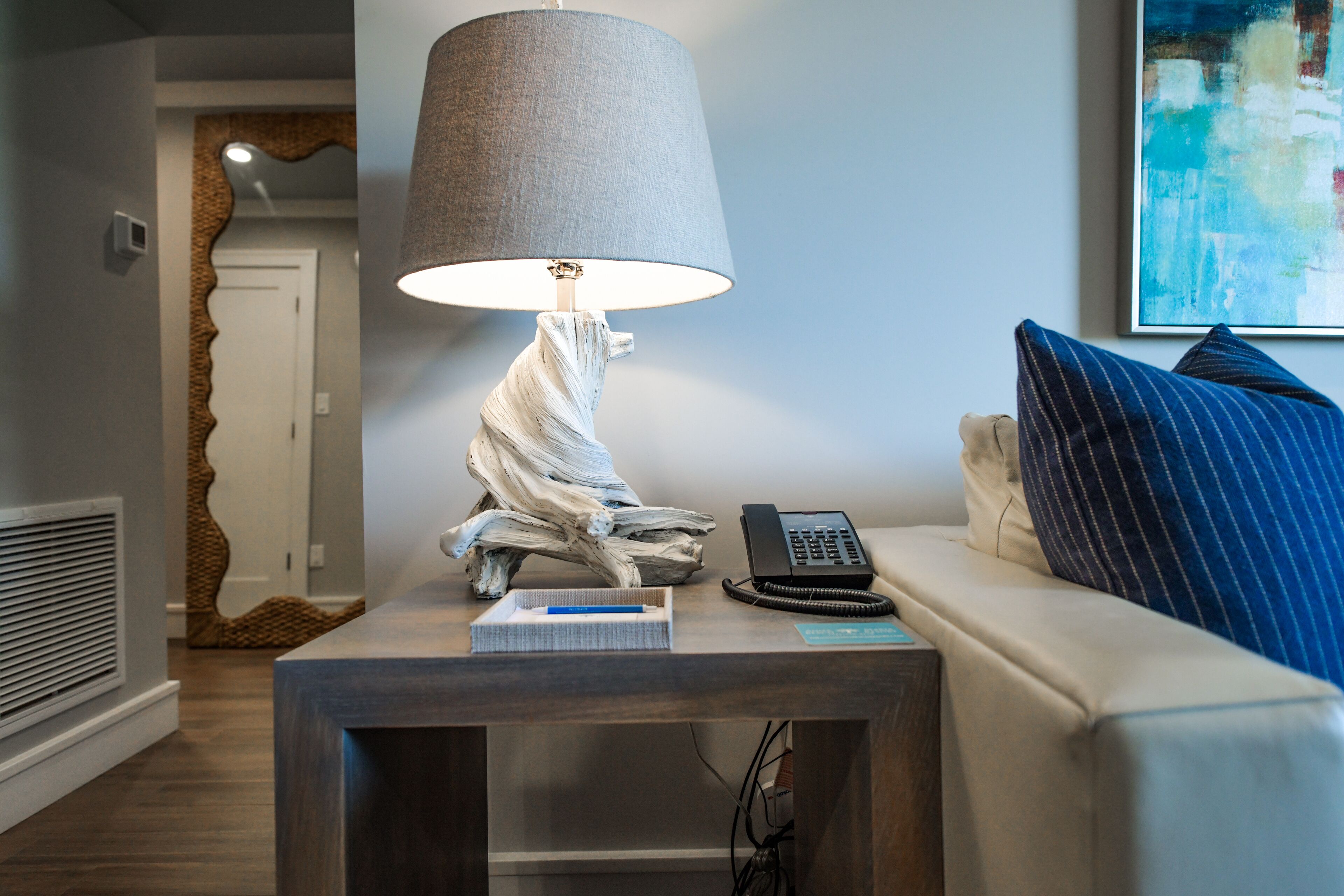 A modern living room with a wooden side table, a lamp, a telephone, and a blue-striped pillow on a sofa.