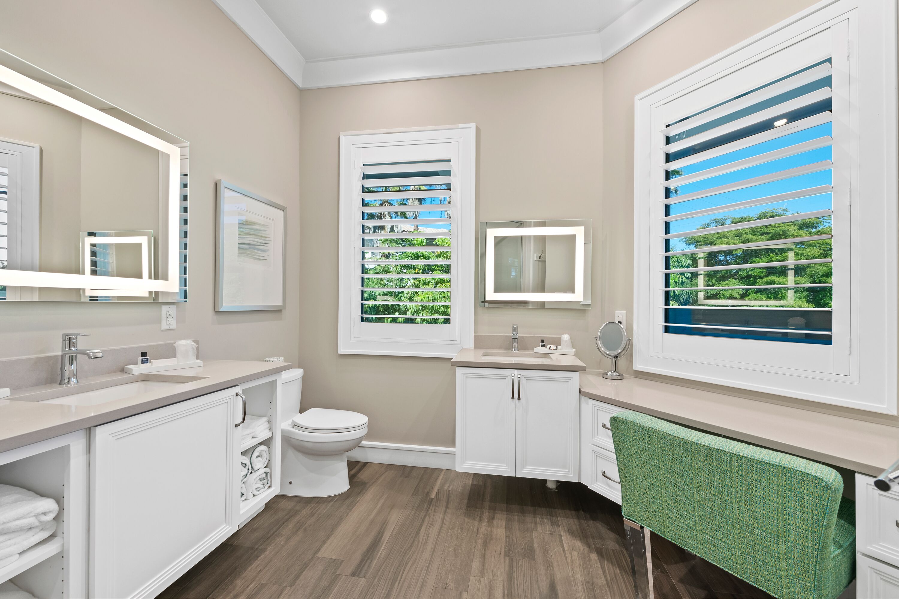 Une salle de bain moderne équipée de toilettes, d’un lavabo, d’un meuble-lavabo et de grandes fenêtres avec stores.