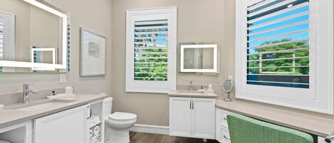 Une salle de bain moderne équipée de toilettes, d’un lavabo, d’un meuble-lavabo et de grandes fenêtres avec stores.