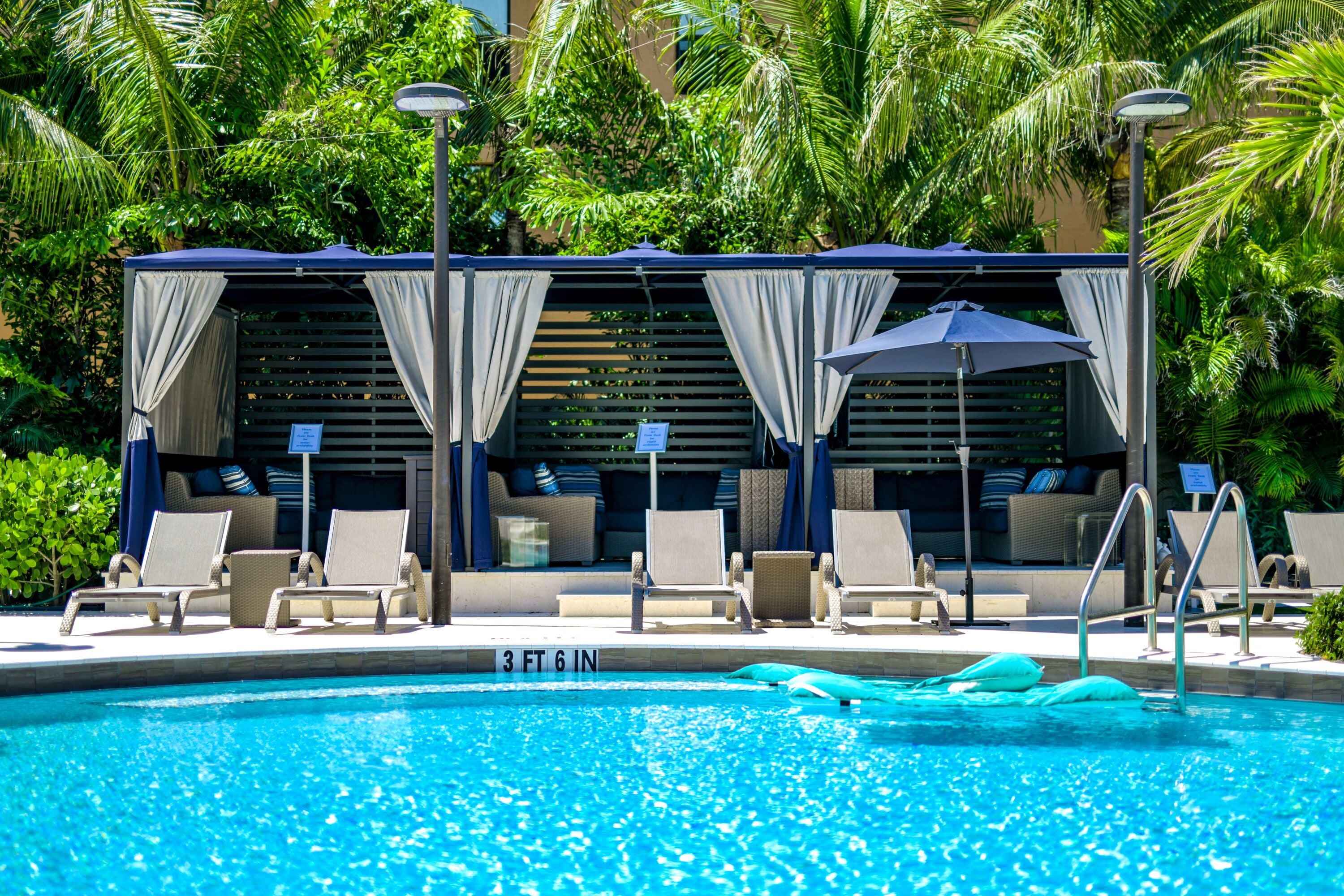 A pool area with lounge chairs, umbrellas, and a covered seating area with curtains.