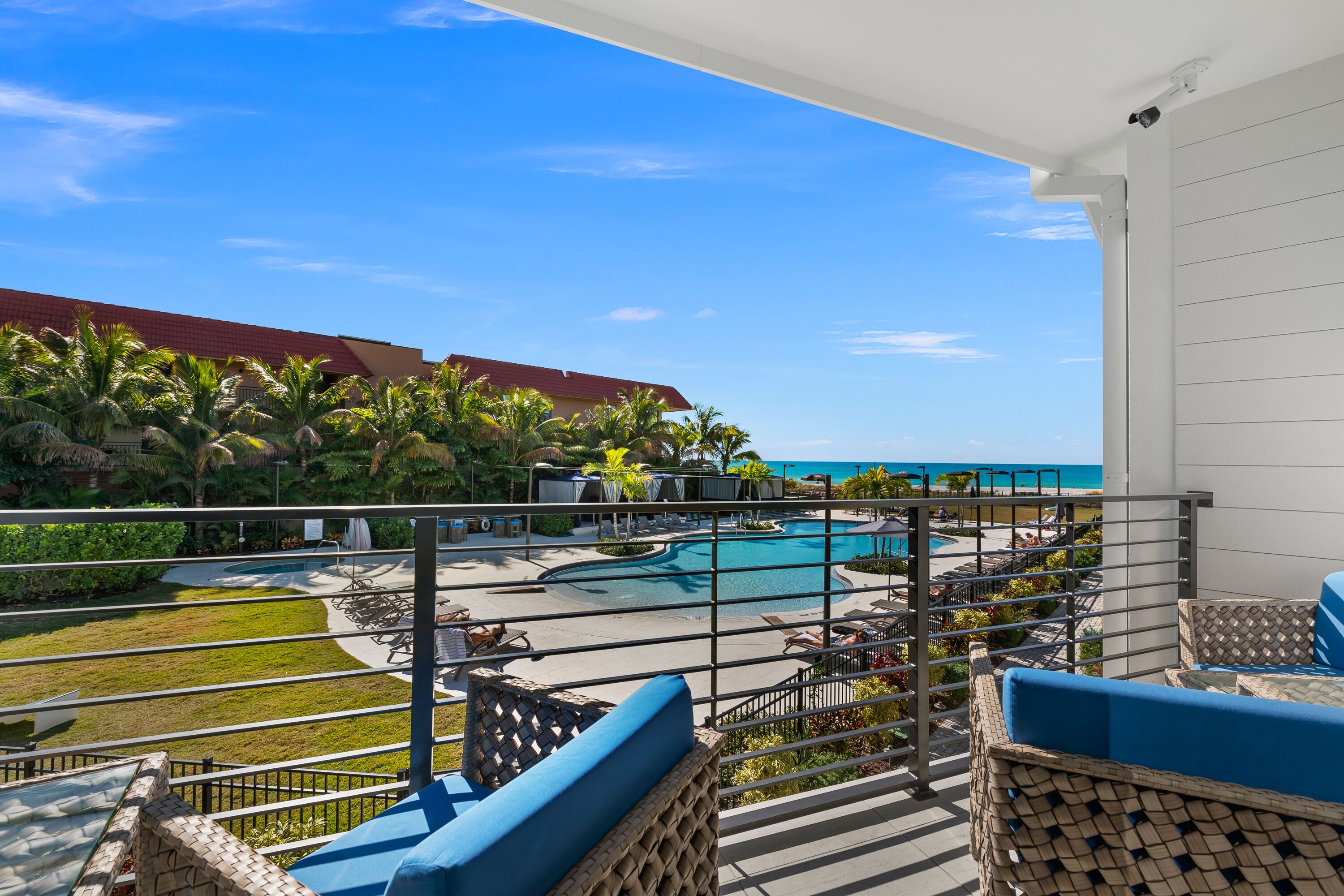 A balcony with wicker furniture, a pool area, and a view of the ocean.