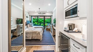 A modern hotel room with a bed, a kitchenette, a ceiling fan, and a large window with a view of greenery. - Anna Maria Beach Resort (Holmes Beach)