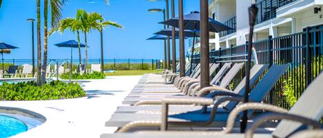 A poolside area with lounge chairs, umbrellas, and a building with balconies.