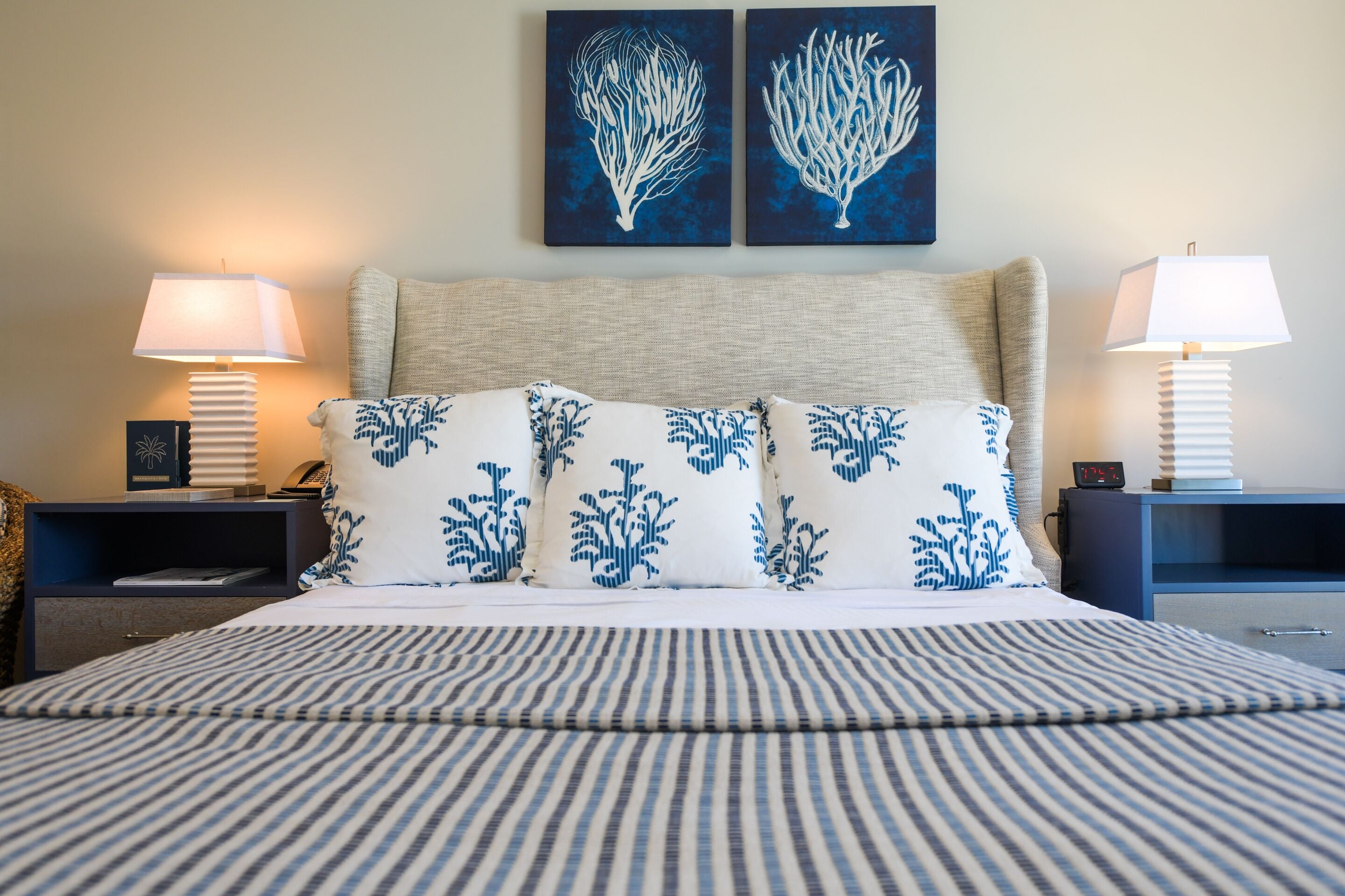 A neatly made bed with striped bedding, two wall-mounted paintings, and bedside lamps on either side.