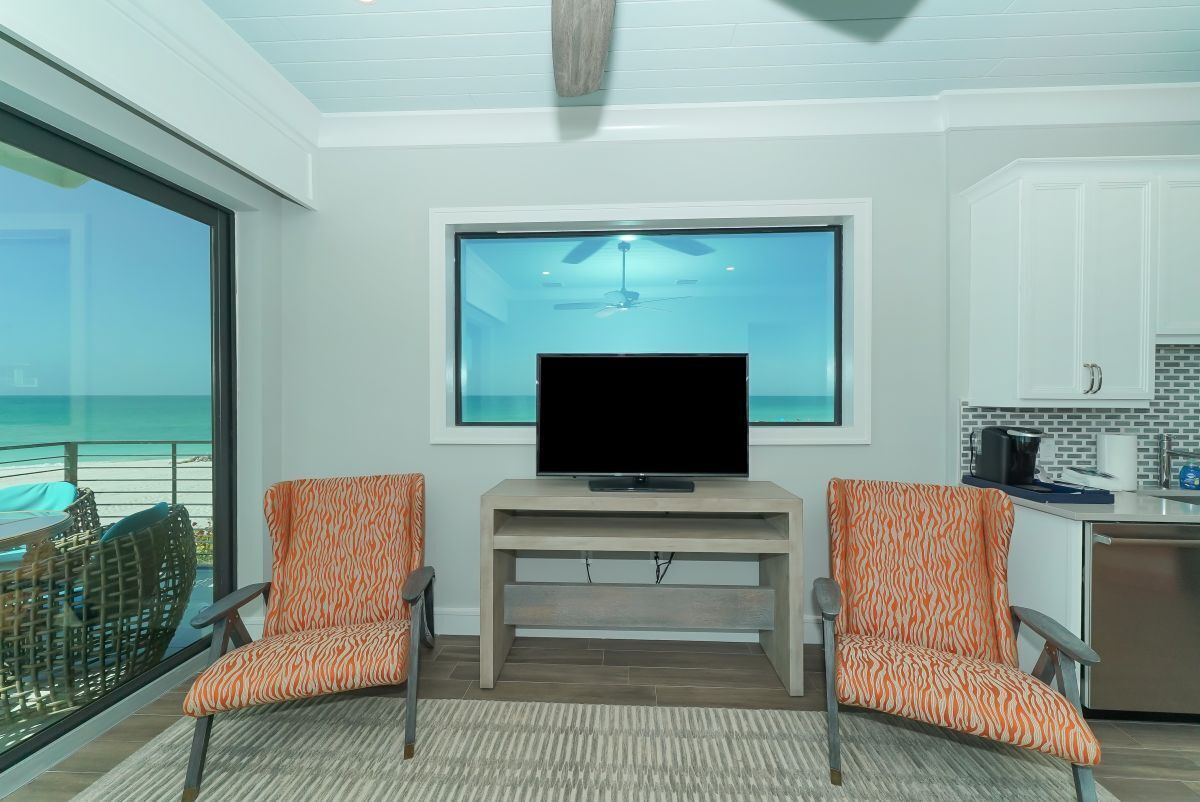 Ein modernes Wohnzimmer mit großem Fernseher, zwei gemusterten Sesseln, einer Holzunterhaltungsecke und Blick auf den Ozean.