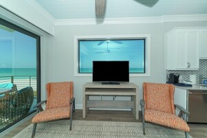 Un soggiorno moderno con una grande TV, due poltrone a fantasia, un mobile TV in legno e vista sull'oceano.