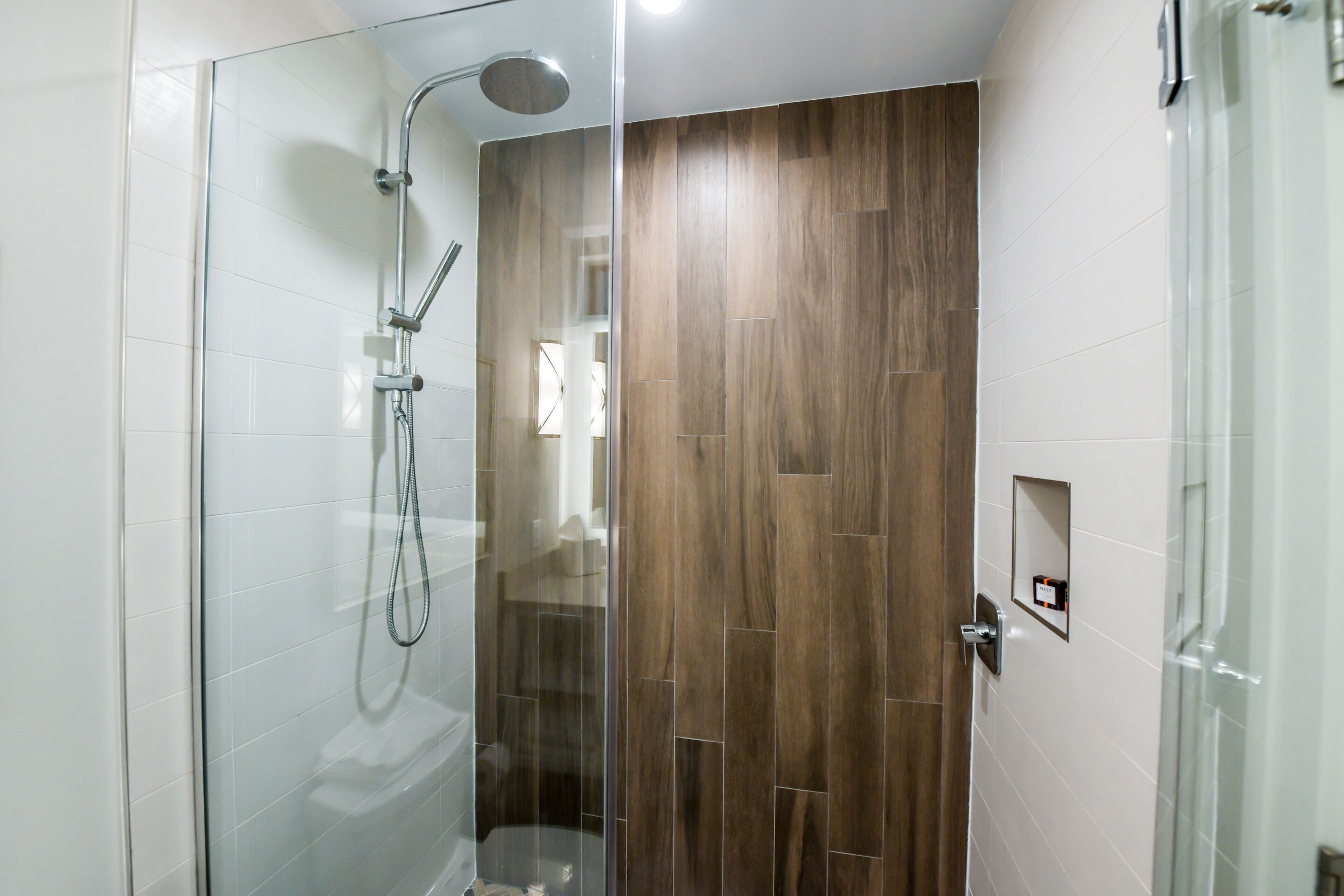 A modern bathroom with a glass shower enclosure, a wooden panel wall, and a white tiled floor.