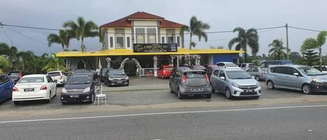 A building with a yellow facade and a red roof, surrounded by parked cars and palm trees.