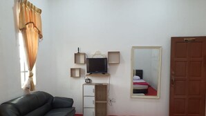 A room with a black leather sofa, a flat-screen TV on a wooden stand, a mirror on the wall, and a door with a sign above it. - Hotel O Z Dirgahayu 313 (Kota Bharu)