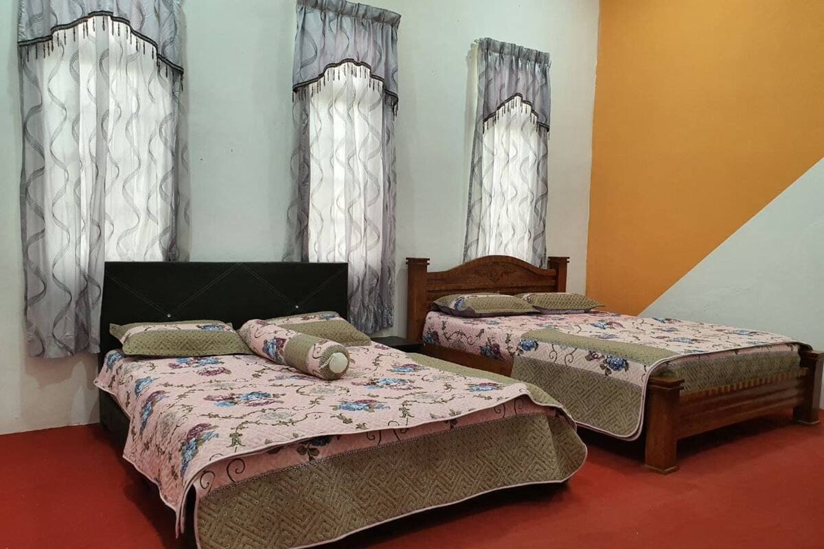 Ein Schlafzimmer mit zwei Einzelbetten, jeweils mit einem blumigen Bettbezug und Kissen. Der Raum verfügt über einen roten Teppich und ein hölzernes Kopfende.