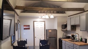 A kitchen with wooden beams, a dining table with chairs, a refrigerator, and a sink. - LVBar Ranch - Cabin #2 (Cane Beds)