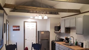 A kitchen with a wooden ceiling, a dining table with chairs, a refrigerator, a stove, and cabinets. - LVBar Ranch - Cabin #2 (Cane Beds)