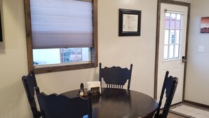 A dining area with a round table and four chairs, a window with blinds, a framed picture on the wall, and a door with a window. - LVBar Ranch - Cabin #2 (Cane Beds)