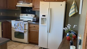 Une cuisine avec des meubles de rangement en bois, une cuisinière blanche, un réfrigérateur blanc et une table en bois sur laquelle est posé un vase de fleurs.