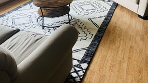 Un salon avec un canapé, une table basse, un téléviseur posé sur un meuble, un tapis à motifs et un tableau accroché au mur.