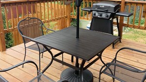 Une terrasse avec une table et des chaises en métal, un barbecue et un auvent.