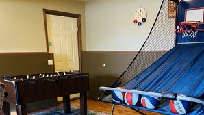 Une pièce équipée d’un baby-foot, d’un trampoline avec des ballons de basket et d’un panier de basket.