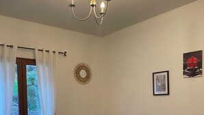Una stanza con un tavolo da pranzo, sedie, un divano, un lampadario e vista attraverso una finestra con tende.