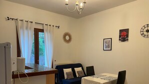 Un ambiente compatto con angolo cottura, un tavolo da pranzo con sedie, un divano e un orologio decorativo a parete.