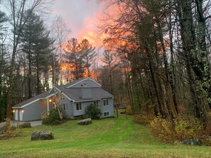 A two-story house with a sloped roof, surrounded by a forested area.