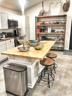 A kitchen with white cabinets, a wooden countertop, a sink, a trash can, and a shelf with various items. - Cozy with plenty of room (Saint John)