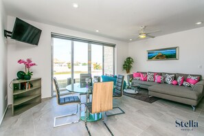 A modern living room with a glass dining table, a sofa, and a TV mounted on the wall. - Marea 34 Tulum by Stella Rentals (Playa del Carmen)