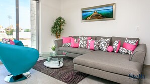 Una sala de estar moderna con un sofá gris, un sillón verde azulado y una mesa de centro de vidrio.